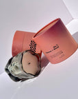 Smoky gray wavy glass candle tilted against two open pink boxes