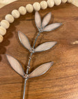 Peachy pink stained glass leaf sprig on a wooden tray beside a wooden bead garland