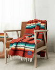 Red-orange sarape with turquoise, black and white stripes draped over a wooden armchair