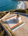 Person sitting on a cream striped blanket on a stone overlook above the ocean