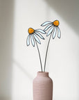 Two pale blue stained glass coneflowers with orange centers in a pink vase