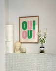 Say it twice with this bold Oui Oui art print. Pink and green text on a clean neutral background adds playful charm to any bathroom or gallery wall.