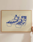 Framed Swim Club print of two women on lounge chairs in blue line art on yellow, being hung on a wall