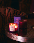 Lit Nueve Leones candle and a dark red candle on a round marble table with a purple box behind
