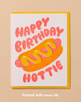 Send some sizzle with this adorable hot dog birthday card, where neon red and yellow inks cleverly overlap to form a tasty bun. The card playfully says, "Happy birthday, hottie," alongside a fun hot dog illustration. 