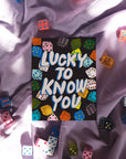 Card with 'Lucky to Know You' text surrounded by colorful dice on a textured surface