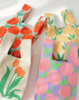 Several floral knit bags in cream, pink and yellow prints piled together