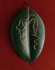 A pair of delicate gold chain necklaces draped over a dark green leaf, set against a textured dark red background.