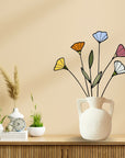 Stained glass wildflowers in a white handled vase on a wooden console beside plants
