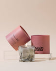 Smoky gray wavy glass candle in front of stacked pink boxes on a clear riser