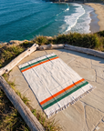 Cream blanket with green and orange stripes spread on a stone overlook above the ocean