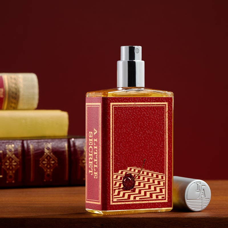 A Little Secret full-size glass bottle with a red label on a wooden table beside old leather-bound books