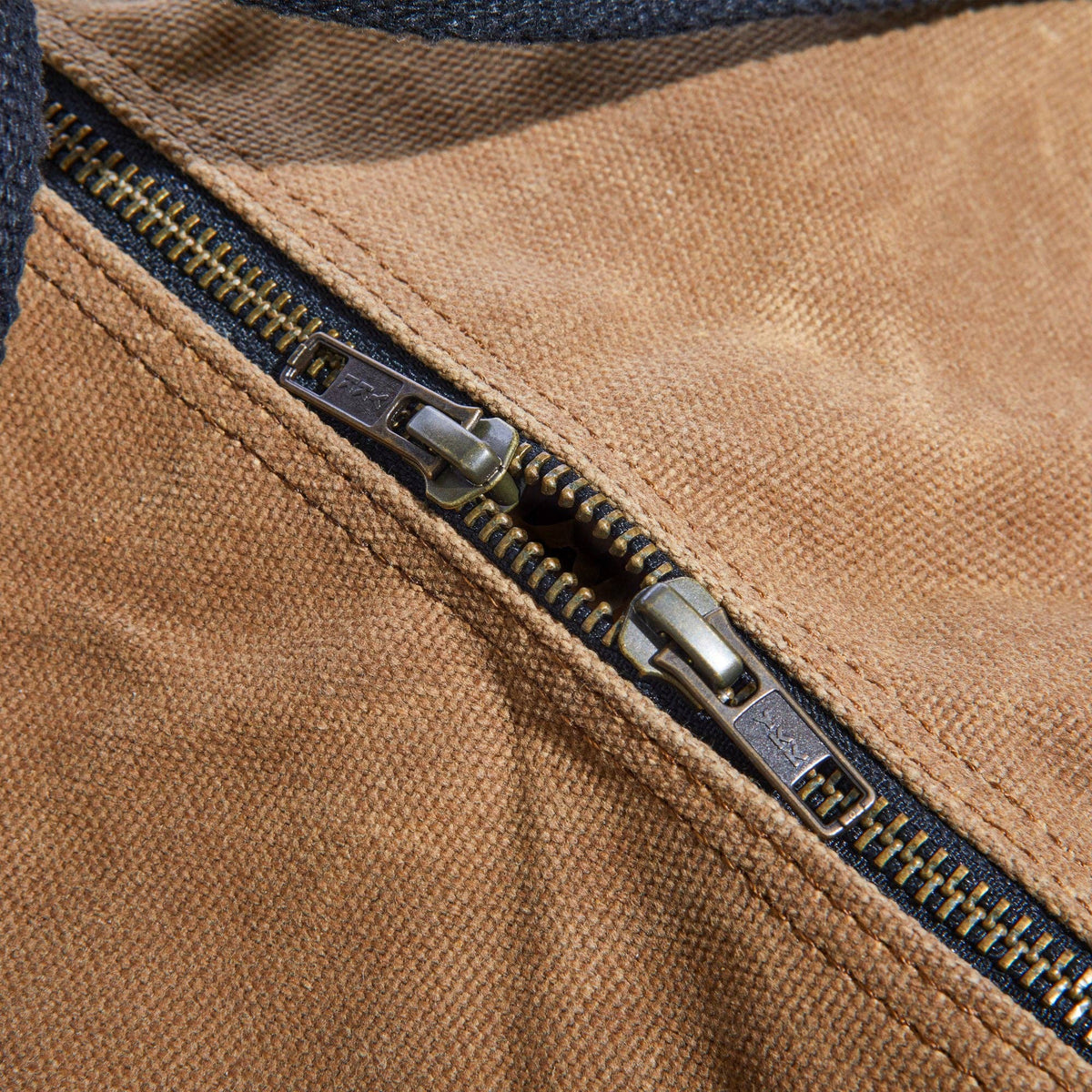 Close-up of the brass zippers on the tan waxed canvas duffel bag