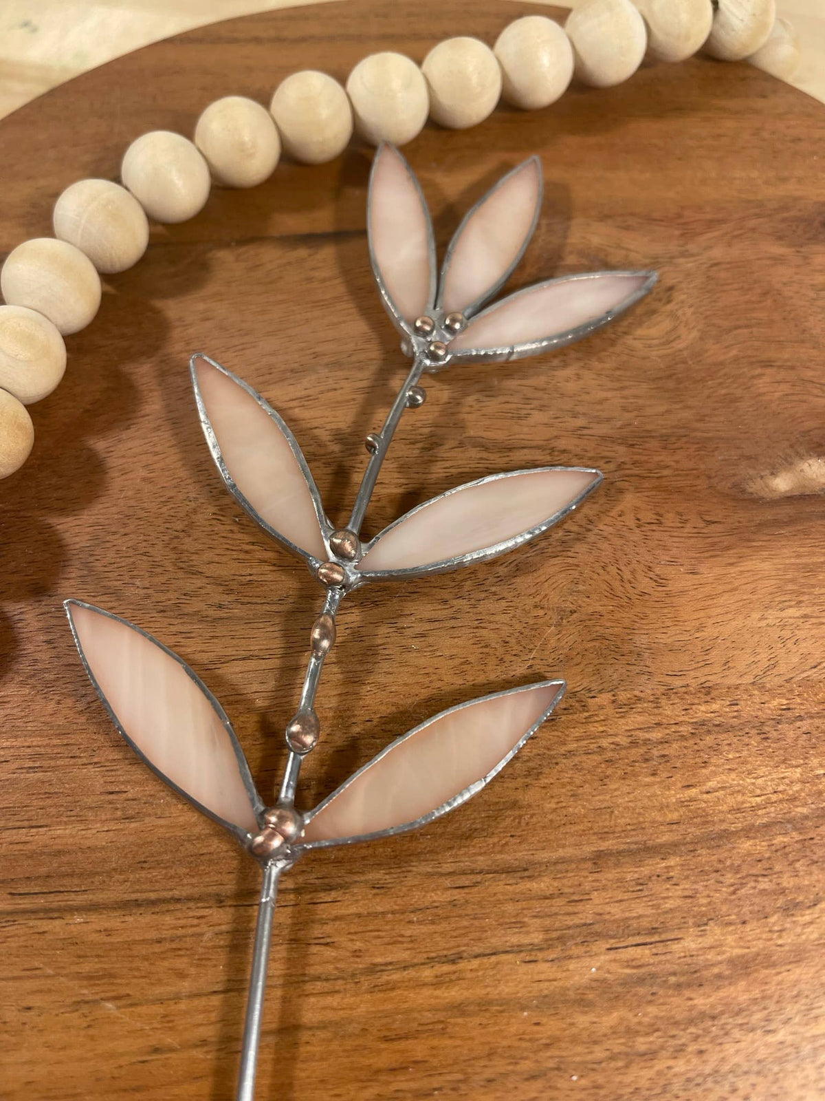 Peachy pink stained glass leaf sprig on a wooden tray beside a wooden bead garland