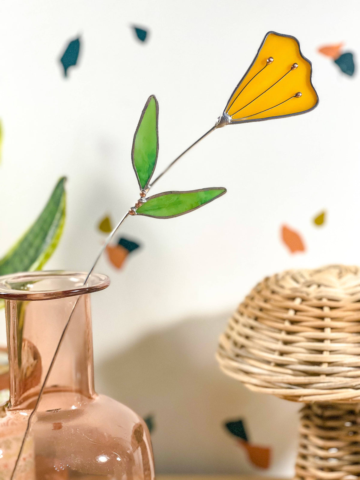 Stained glass yellow tulip stem in a pink glass bottle next to a woven basket