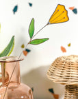 Stained glass yellow tulip stem in a pink glass bottle next to a woven basket