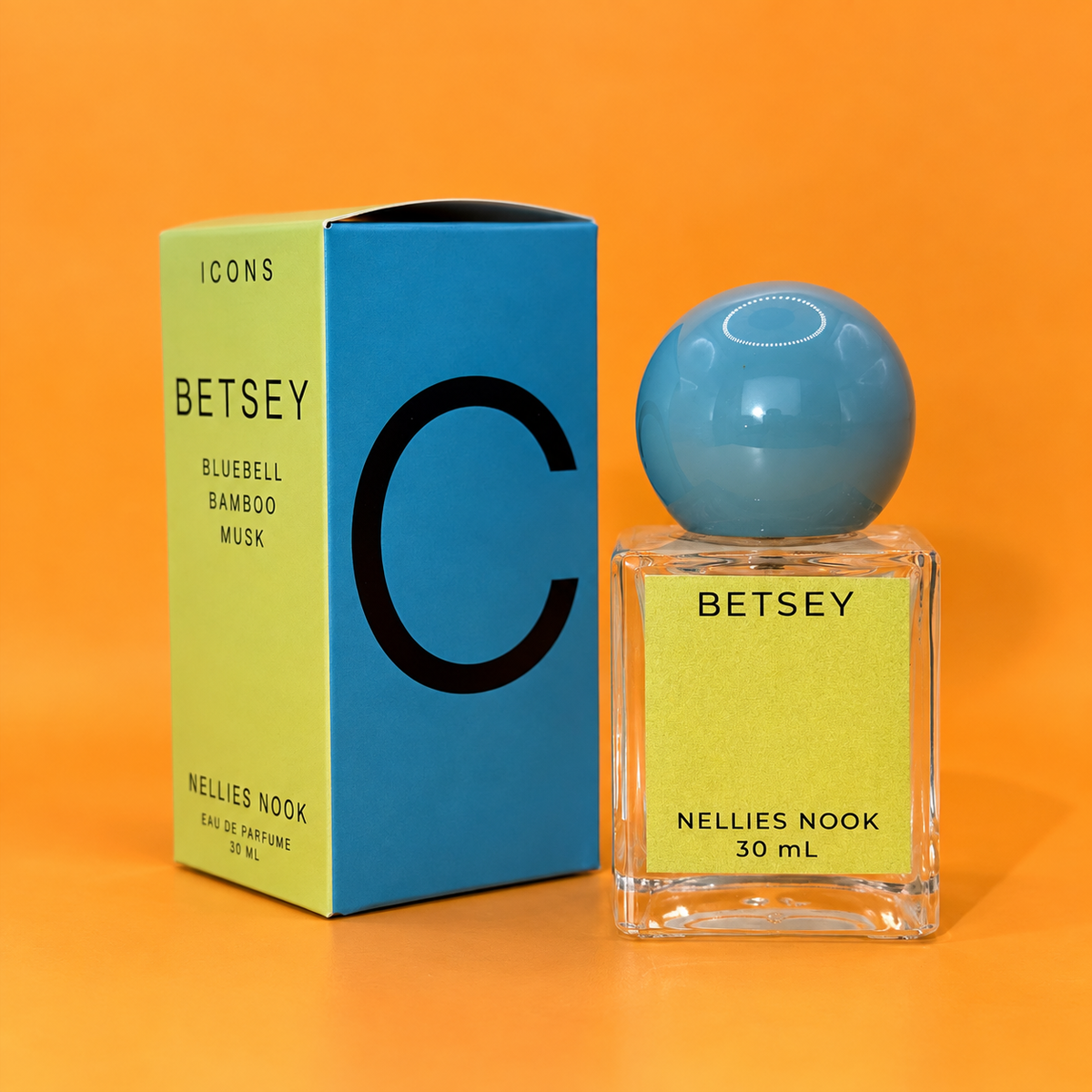 Green and blue Icons Betsey box beside a glass perfume bottle with a light blue sphere cap and green label, on an orange background