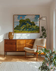 Framed live oak print on a white wall above a wood sideboard and lounge chair
