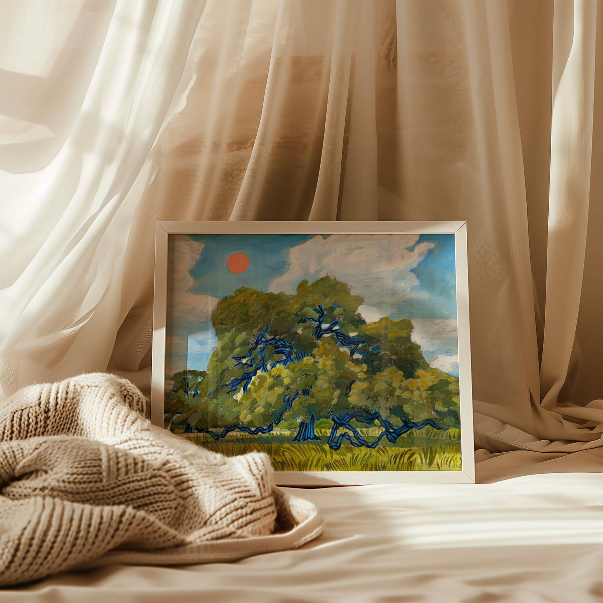 Framed live oak print resting on cream bedding with sheer curtains behind