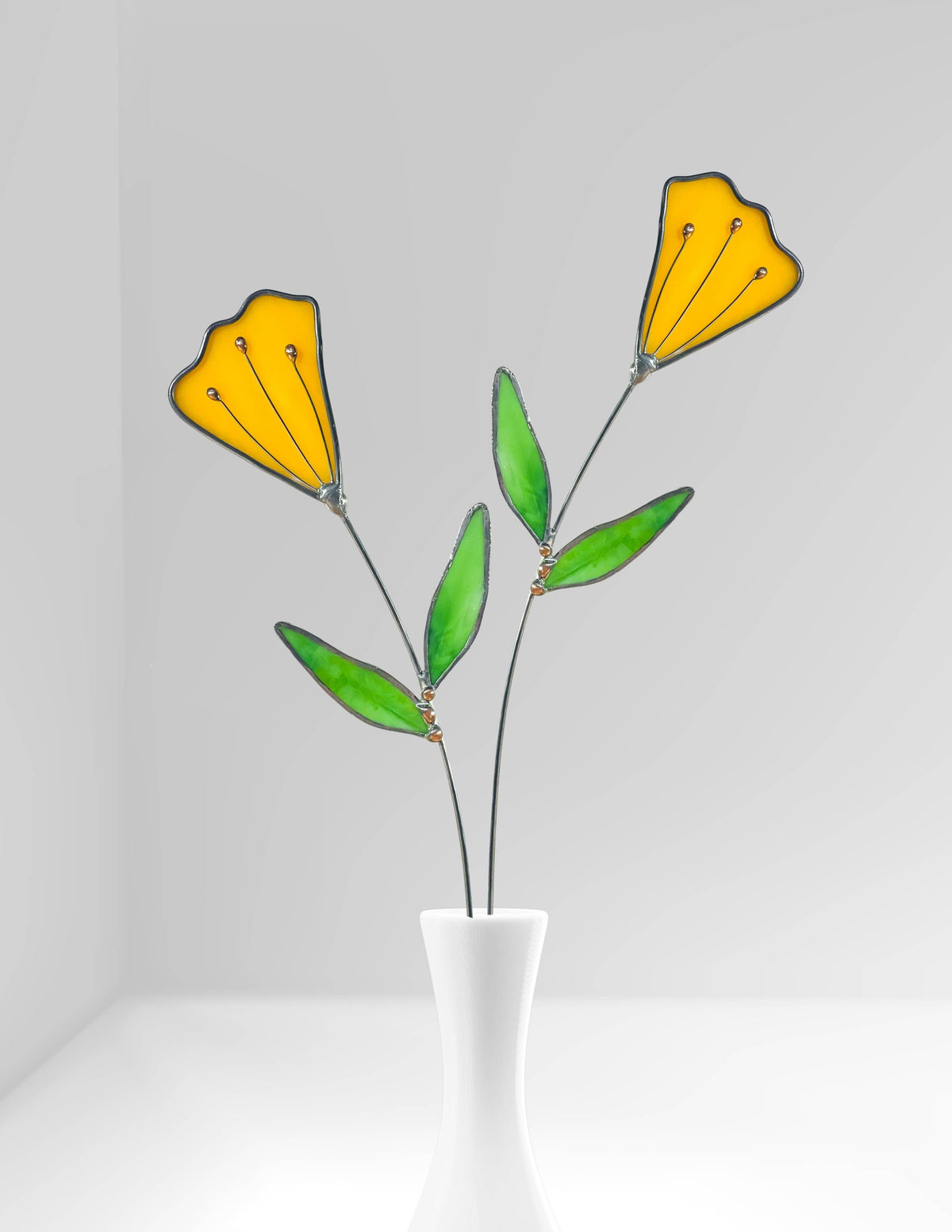 Two stained glass yellow tulip stems in a white bud vase