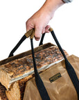 Hand lifting the firewood carrier by its canvas-wrapped handles over a stack of logs