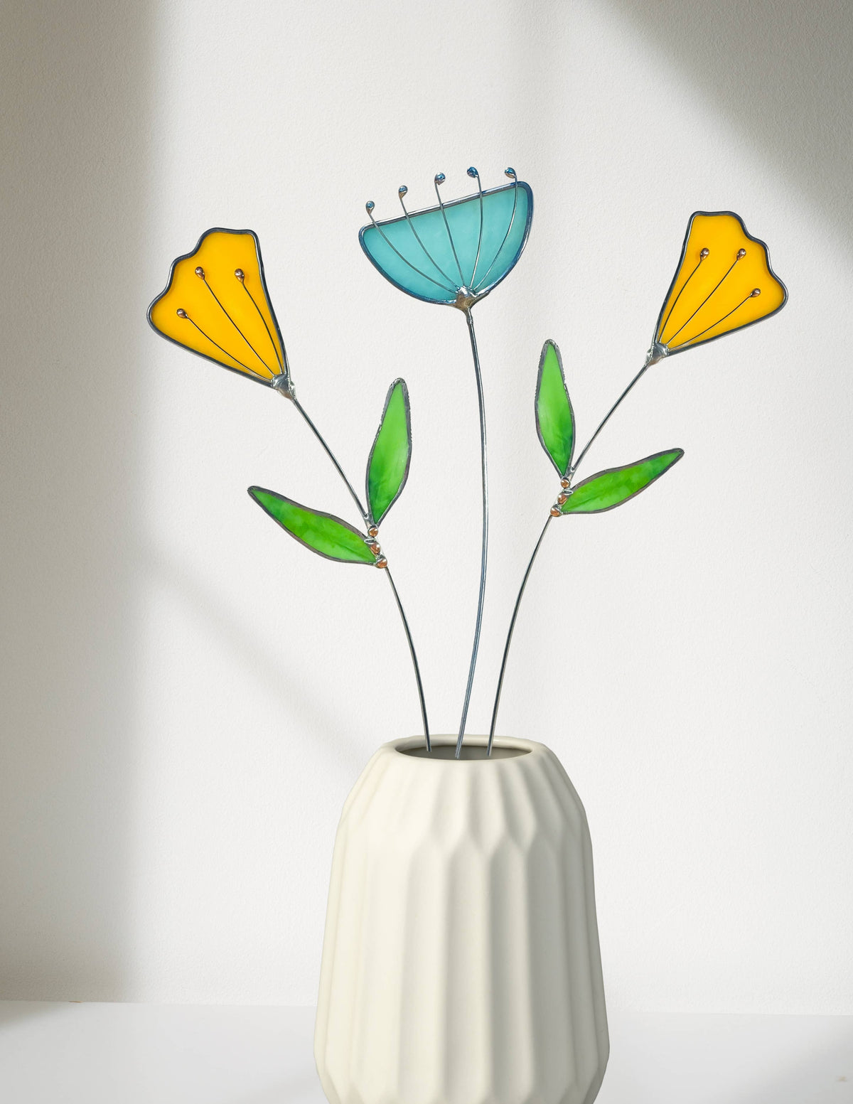 Two stained glass yellow tulips and an aqua flower in a white ribbed vase