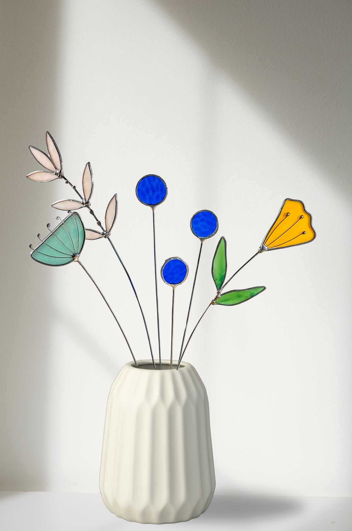 Stained glass yellow tulip with blue, aqua and sprig stems in a white ribbed vase