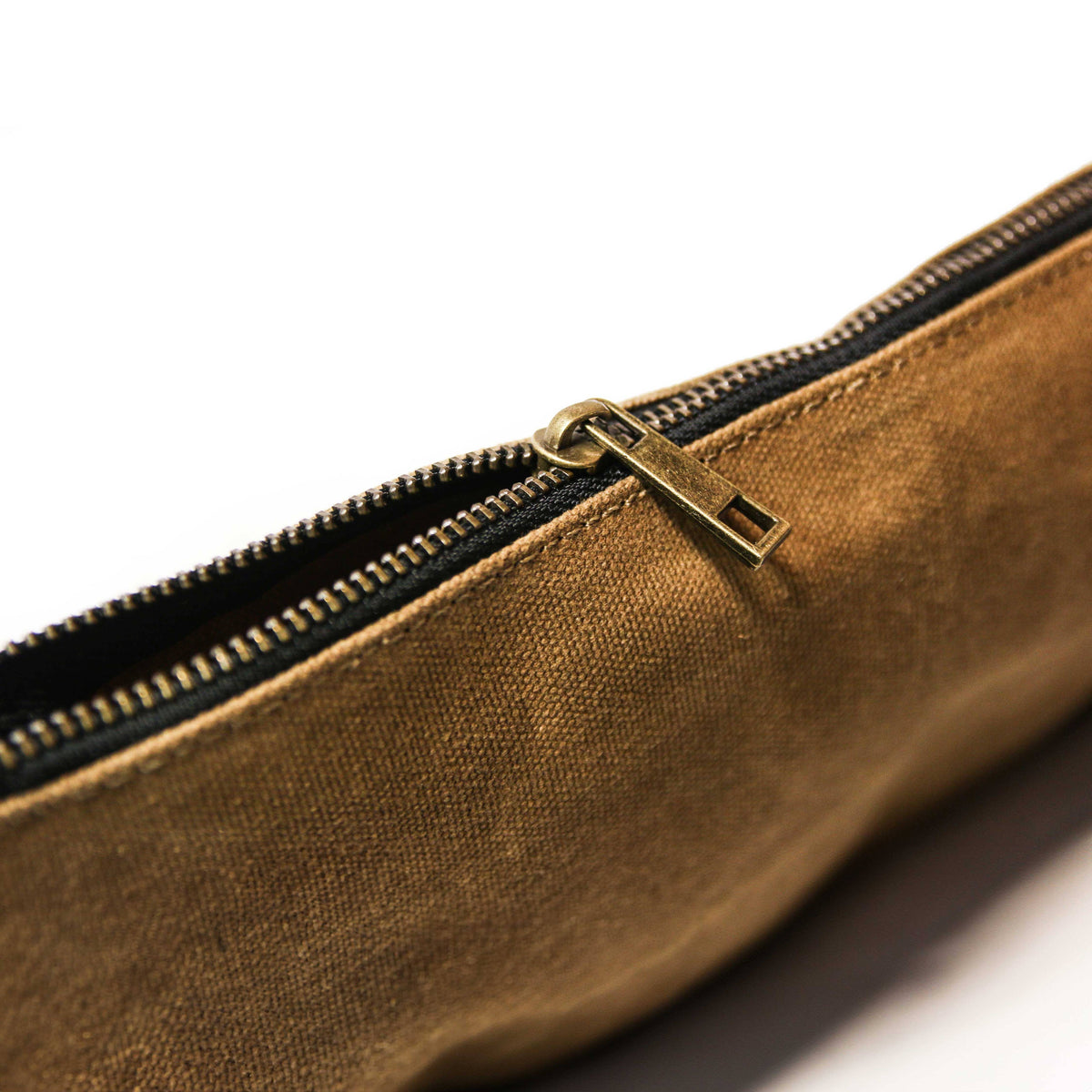 Close-up of the brass zipper pull on a tan waxed canvas bag