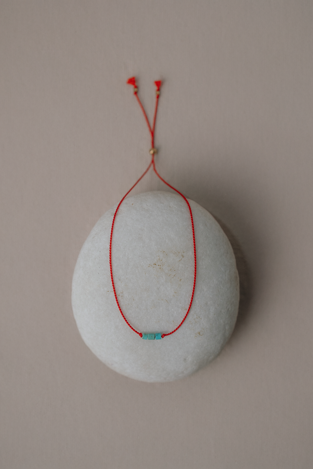 Round stone with red string and turquoise bead on a beige background