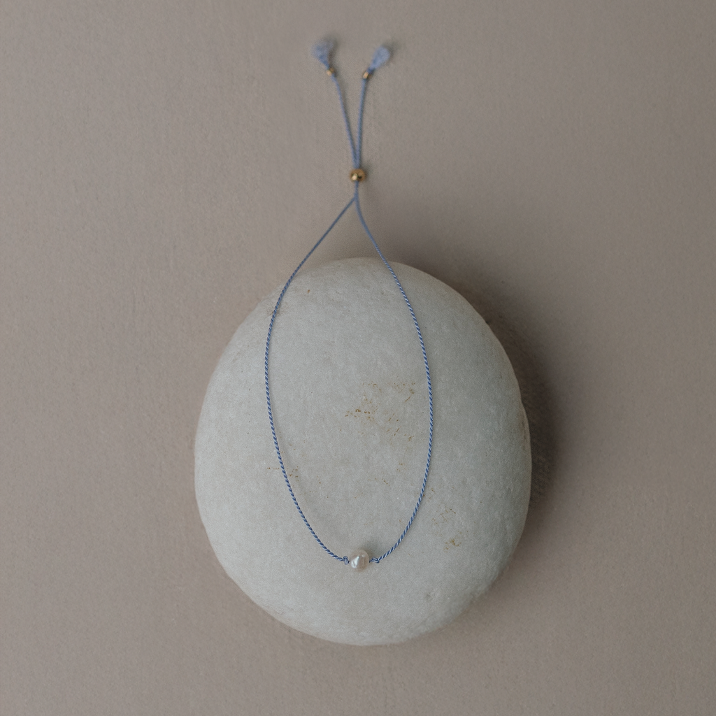 Blue string necklace with a small pendant on a gray stone surface