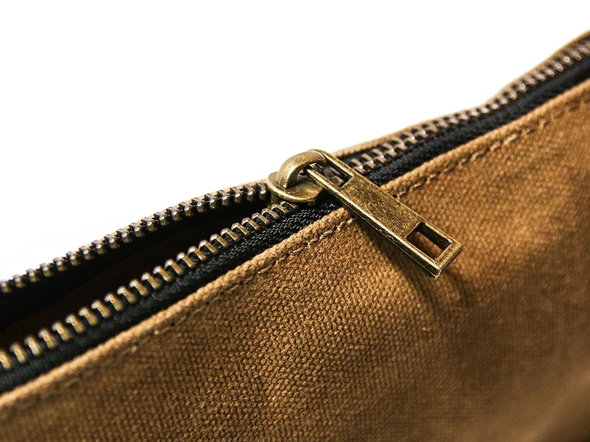Close-up of a brass zipper pull on tan waxed canvas, slightly unzipped