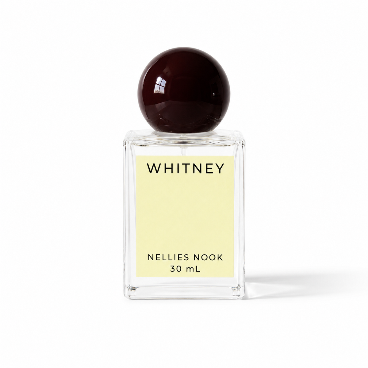 Whitney perfume bottle with a dark burgundy sphere cap and pale yellow label on a white background