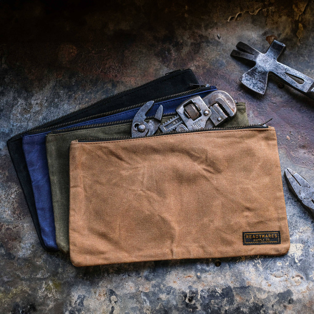 Waxed canvas zipper tool bags in tan, olive, navy and black with wrenches and a hammer on a rusty metal surface