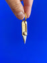 Fingers holding a small brass craft knife keychain against a blue background