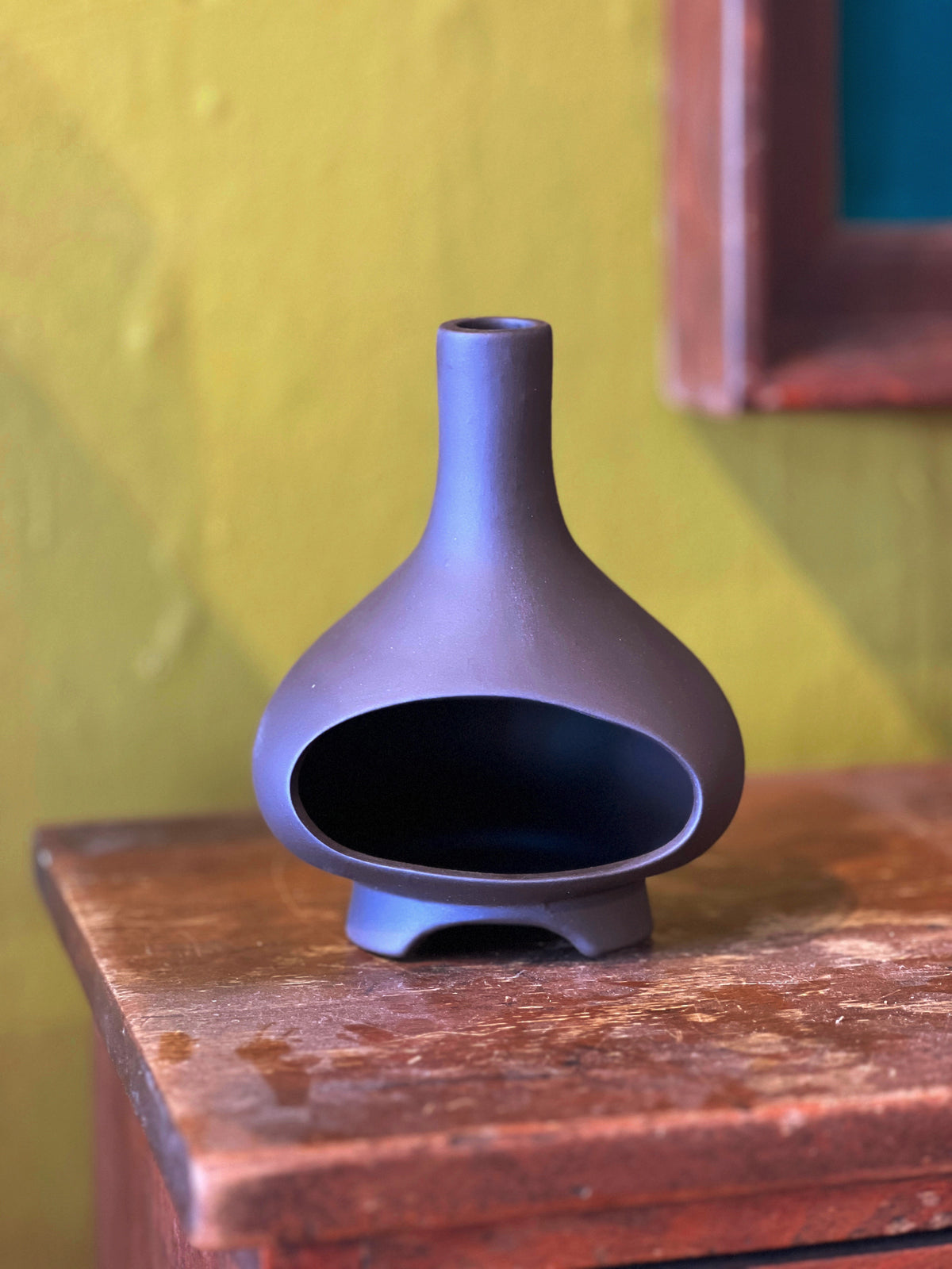 Dark charcoal ceramic chiminea incense holder on a wood table against a yellow wall