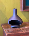 Dark charcoal ceramic chiminea incense holder on a wood table against a yellow wall