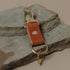 Brass clip fob with a tan leather strap resting on a flat stone