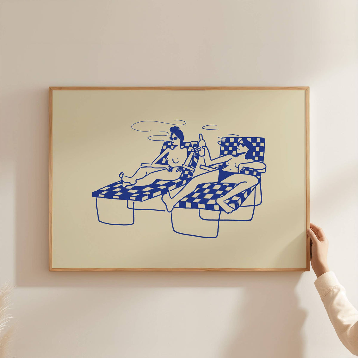 Framed Swim Club print of two women on lounge chairs in blue line art on yellow, being hung on a wall