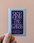Card deck with 'Ask the Cards' text held by a hand against a pink background