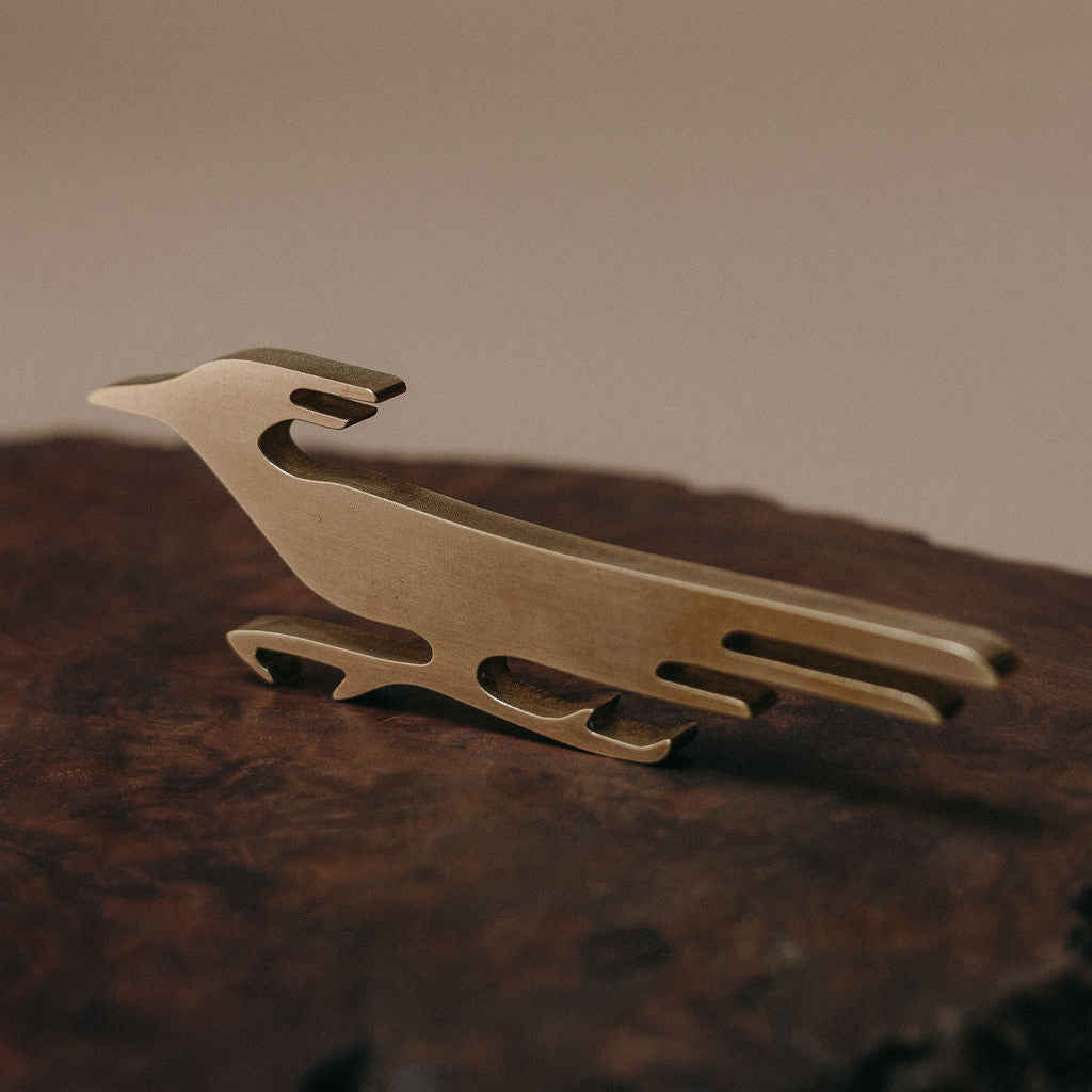 A small brass bird-shaped decorative object resting on a dark textured wooden surface against a soft beige background.