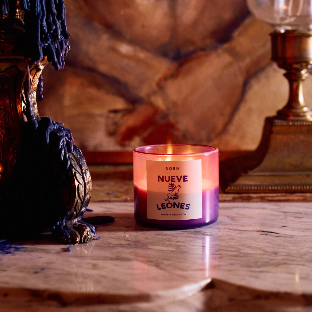 Lit ROEN Nueve Leones candle in a hand-painted purple jar on a marble table in a dim room
