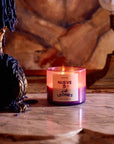 Lit ROEN Nueve Leones candle in a hand-painted purple jar on a marble table in a dim room