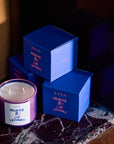 Nueve Leones candle in a painted jar next to stacked blue ROEN boxes on marble