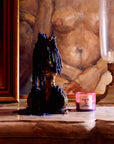 Small lit Nueve Leones candle on a marble mantel beside a dark figurine and a glass lamp