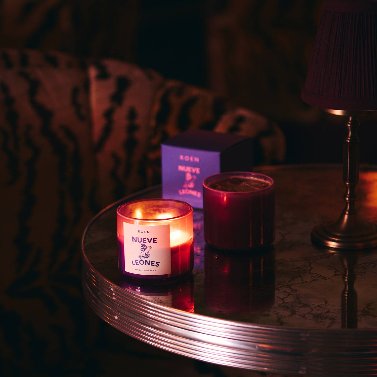 Lit Nueve Leones candle and a dark red candle on a round marble table with a purple box behind