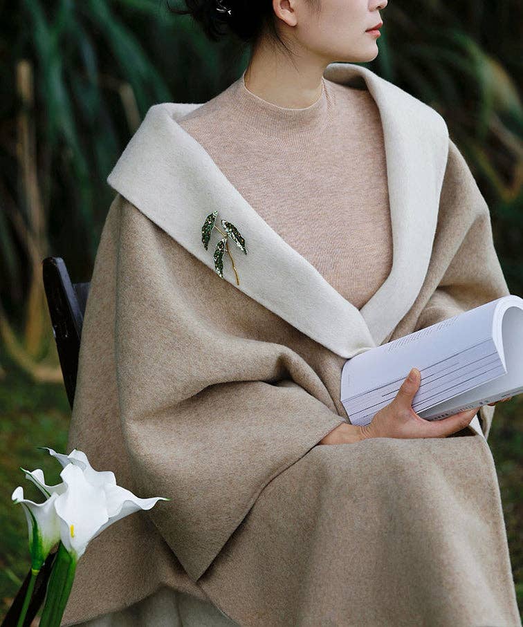 Person wearing a beige coat with a white flower and book in the foreground