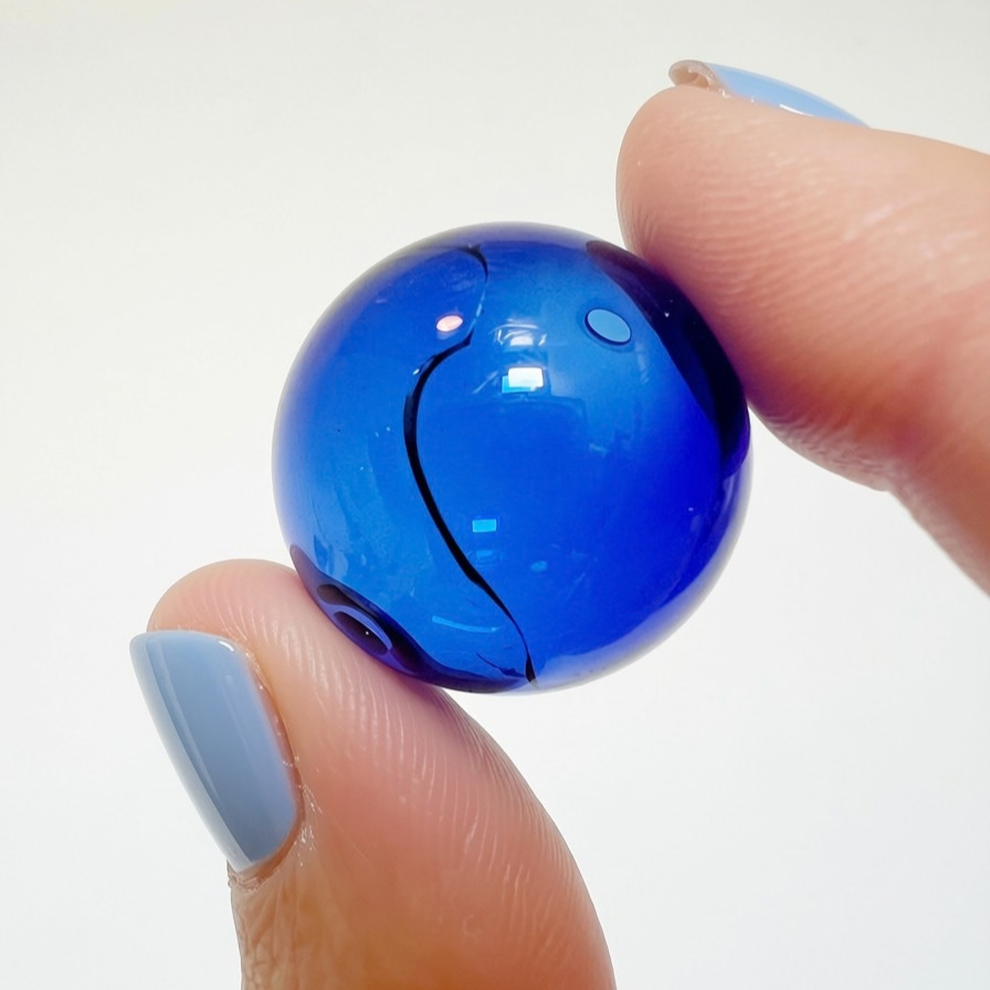 Fingers holding a cracked blue hand-blown glass sphere