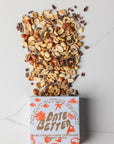 Box of Date Better chocolate with a scattering of nuts and seeds on a light background