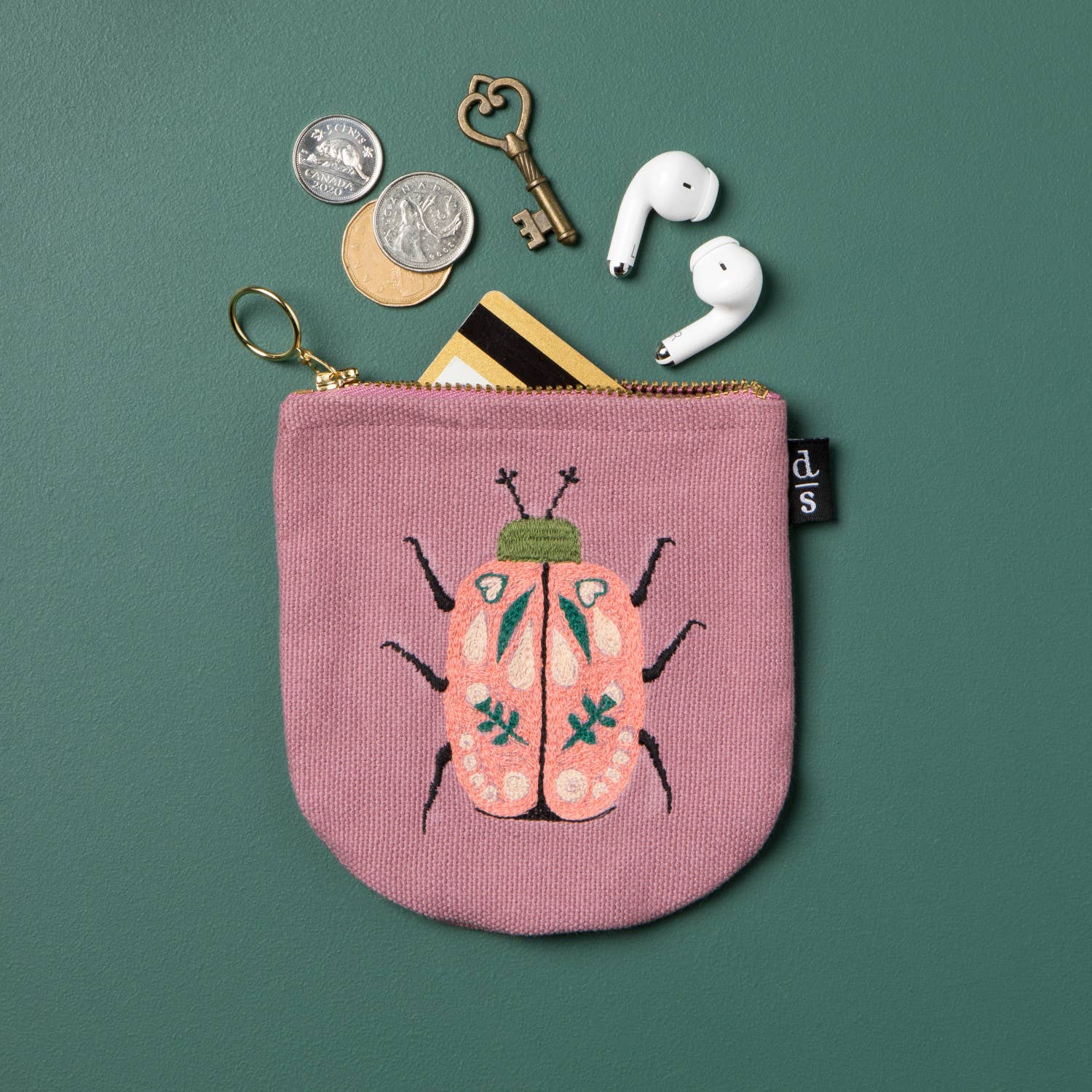 Secure your small valuables in the Amulet Halfmoon Pouch. Featuring a scarab beetle design on deep musky pink, perfect for keys, cards, and loose coins.