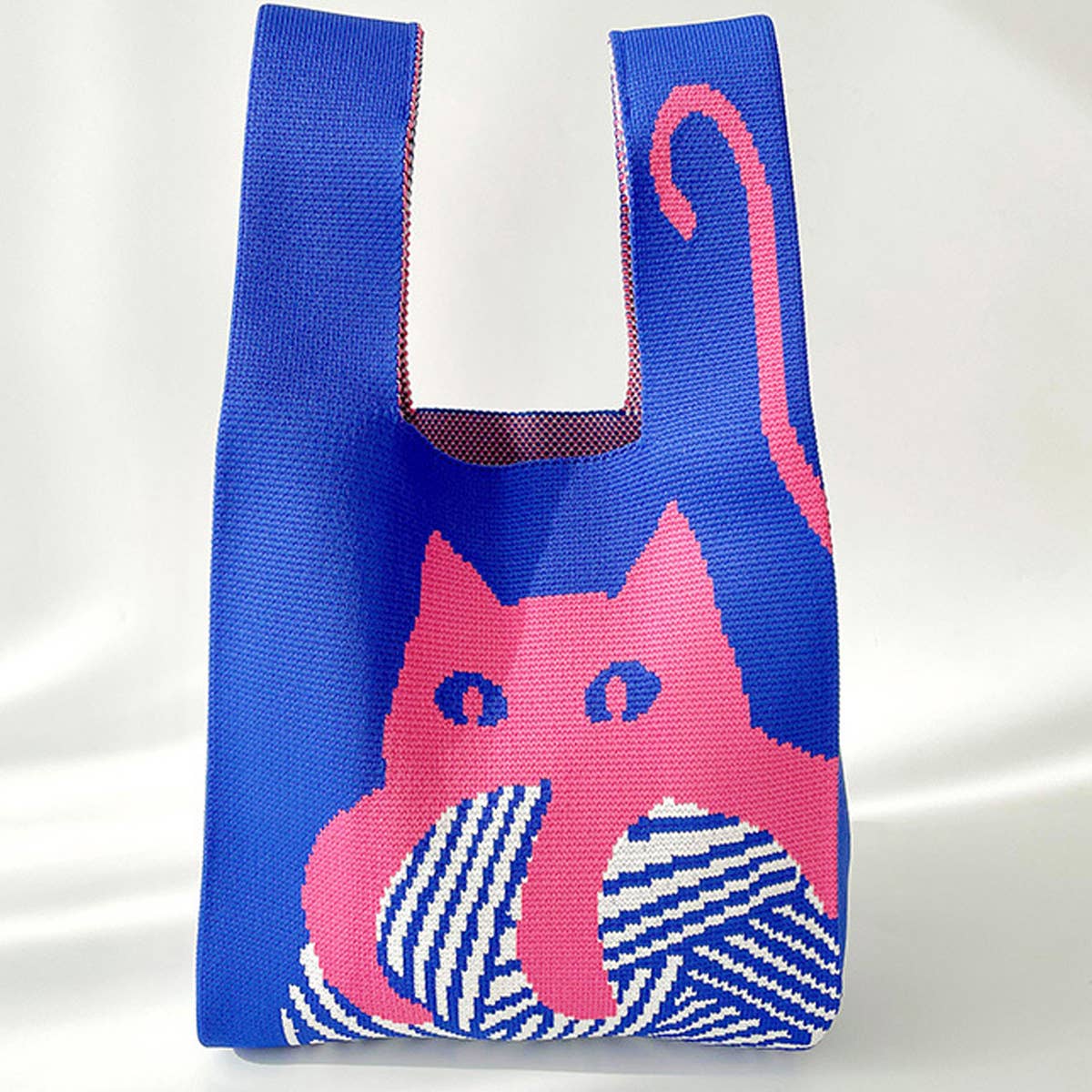 Blue knit shoulder bag with a pink cat on a ball of yarn, on a white backdrop